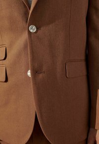 Brauner Lounge-Jacke aus strukturiertem Stoff, mit zwei Fronttaschen, einem einreihigen Knopfverschluss und sichtbaren Steppnähten.