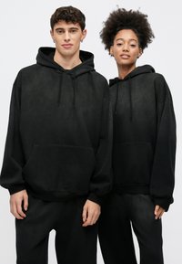 Μαύρα φούτερ με κουκούλα και κορδόνια, ευρύχωρες μπροστινές τσέπες και άνετη εφαρμογή. Κατασκευασμένα από μαλακό ύφασμα, με ελαφρώς υφή επιφάνειες.