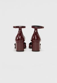 Sandale cu toc înalt din piele lucioasă burgundy, cu curea pentru gleznă, toc pătrat și design cu vârf deschis. Textură netedă și finisaj strălucitor.
