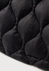 Μαύρο καπιτονέ ύφασμα με διαμαντοειδές μοτίβο, που αναδεικνύει μια μαλακή υφή και γυαλιστερή επιφάνεια. Διαθέτει φουσκωμένα τμήματα για μόνωση.