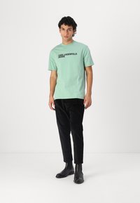 Myntgrønn bomull T-skjorte med korte ermer, med svart tekst "KARL LAGERFELD JEANS". Kombinert med svarte teksturerte bukser og ankelstøvler.