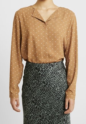 Blusa marrone a pois con scollo a V e maniche lunghe, abbinata a una gonna verde con stampa leopardata e superficie texturizzata.