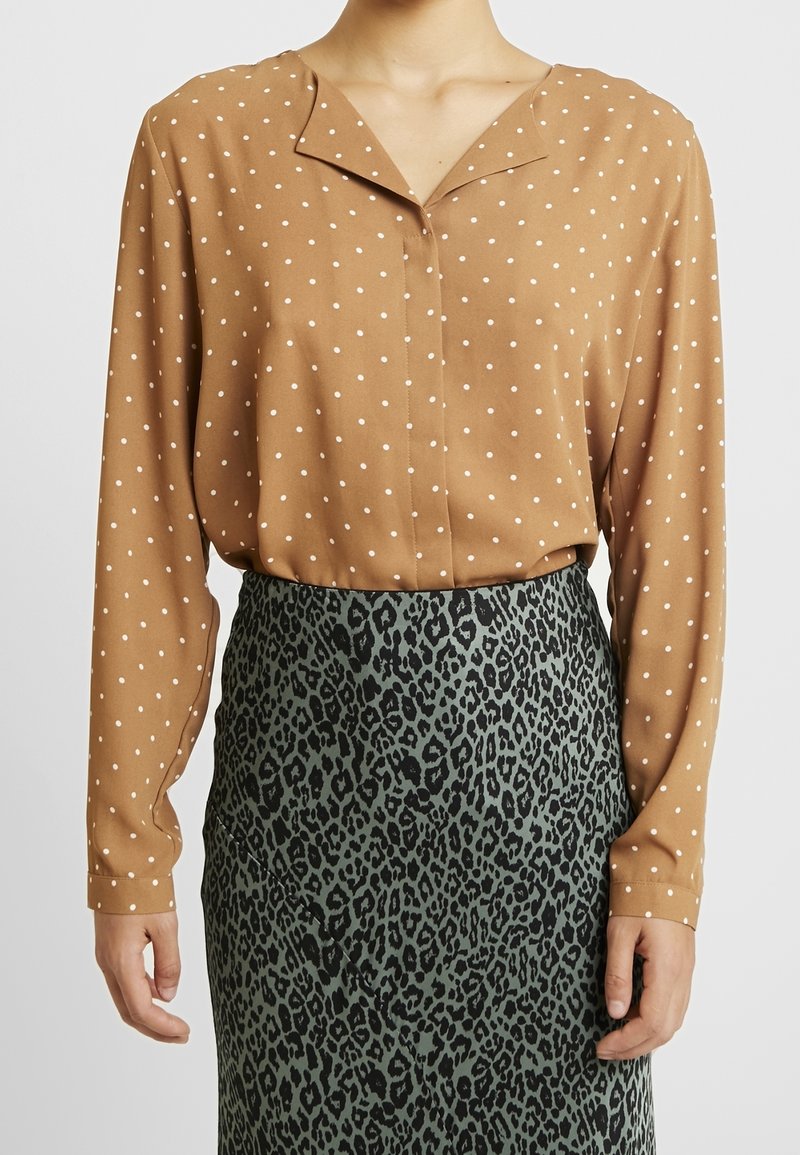 Blusa marrone a pois con scollo a V e maniche lunghe, abbinata a una gonna verde con stampa leopardata e superficie texturizzata.