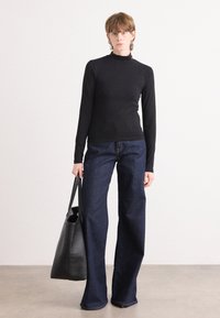 Fekete, hosszú ujjú garbó, széles szárú sötétkék farmernadrággal párosítva. A modell fekete vászontáskát tart. Minimalista dizájn, sima szövettextúra.
