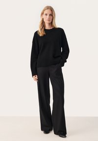 Svart stickad tröja med rundad halsringning, tillsammans med vida svarta byxor. Outfiten har en avslappnad passform och ribbade ärmslut.