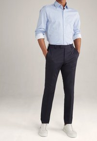 Jasnoniebieska koszula w wzory z podwiniętymi rękawami, w połączeniu z ciemnogranatowymi spodniami i białymi trampkami. Posiada klasyczny kołnierzyk i dopasowany krój.