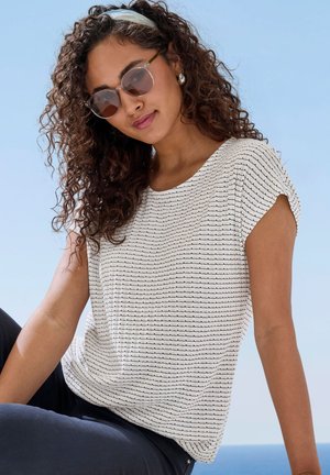 Weißes kurzärmliges Oberteil mit schwarzen horizontalen Streifen, lockerer Schnitt und weichem Material. Kombiniert mit dunklen Hosen und Sonnenbrille. Hintergrund ist der blaue Himmel.