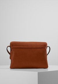 Brun läderhandväska med en slät textur, rektangulär form och två svarta handtag. Har ett lockstängning och en minimalistisk design.