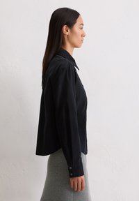 Chemise noire à boutons avec col, manches longues et coupe décontractée. Le tissu semble doux avec une texture lisse.