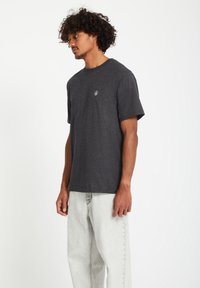 Mannen donkergrijze katoenen T-shirt met ronde hals, korte mouwen en een klein wit logo op de borst, gecombineerd met lichtgrijze losvallende jeans.