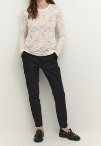 Spetsöverdel med långa ärmar i off-white, prydd med blommönster; tillsammans med skräddarsydda svarta byxor och glänsande svarta loafers.