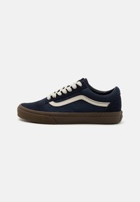 Marineblå kanvassneakers med en hvit sidestripe, rund tå og brun gummisåle. Har hvite snørebånd og polstret krage for komfort.