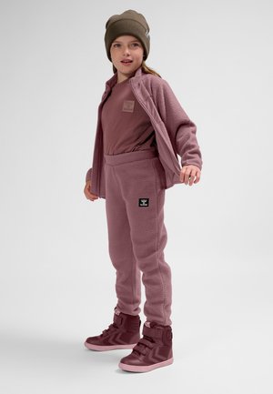 Rosa Fleece-Outfit mit einer Reißverschlussjacke und passenden Hosen, kombiniert mit burgunderroten High-Top-Sneakers und einer braunen Mütze.