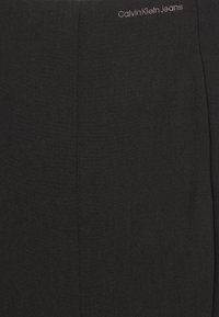 Svarta stretchbyxor med en slät textur. Har en Calvin Klein Jeans-logotyp i subtil grå färg vid midjan. Enkel design, inga mönster.