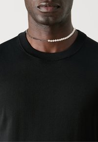Svart strikket genser med ribbestrikket hals. En lagdelt choker har sølvkjede og hvite perler, som gir kontrast.