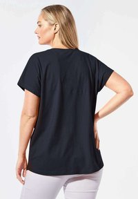 Schwarzes Kurzarm-T-Shirt aus weichem Stoff, mit lockerer Passform und abgerundetem Saum, von hinten betrachtet, das ein schlichtes Design ohne Verzierungen zeigt.