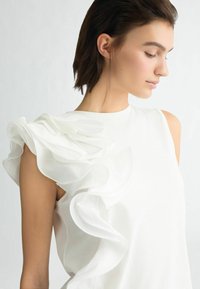 Top bianco senza maniche con dettaglio arricciato su una spalla. Tessuto morbido, design minimalista e silhouette elegante.