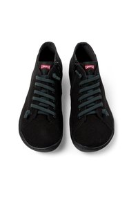 Scarpe da tela nere con lacci verde scuro, punta rotonda e suola di gomma. Presentano una zip su ciascun lato e un'etichetta rossa "Camper" sulla linguetta.