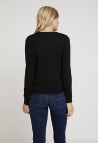 Černý pletený svetr s dlouhými rukávy a kulatým výstřihem, s přiléhavým střihem. Kombinován s tmavě modrými džínami.