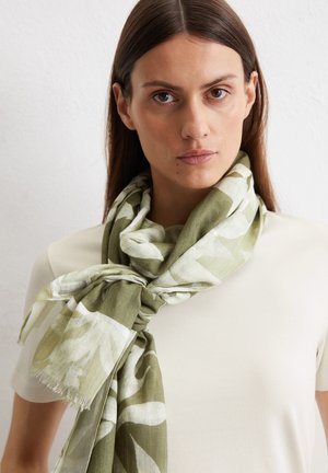 Groene en witte geweven sjaal van lichtgewicht stof, om de nek geknoopt met franjes aan de randen, gedragen over een eenvoudig shirt.