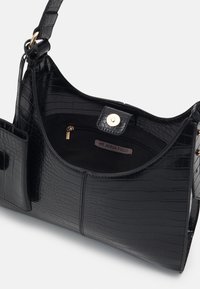 Czarna torebka wykonana z błyszczącego materiału z tłoczonym wzorem krokodyla; posiada zamykaną na zamek kieszeń wewnętrzną, zapięcie na zatrzask oraz przednią kieszeń dla dodatkowej wygody.