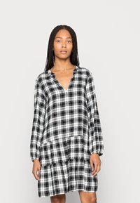 Vestido xadrez preto e branco com mangas longas, decote em forma de V e assimetria com camadas de babados na barra, feito de um tecido macio e leve.