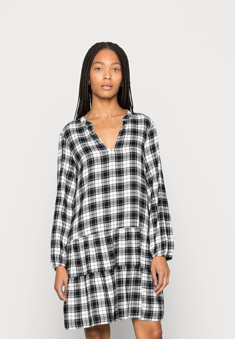 Vestido xadrez preto e branco com mangas longas, decote em forma de V e assimetria com camadas de babados na barra, feito de um tecido macio e leve.