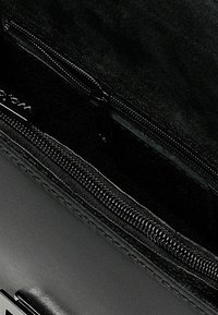 Interno di una borsa a tracolla nera in pelle con una texture liscia, dotato di un comparto con zip e di un sottile etichetta del marchio su uno sfondo scuro.