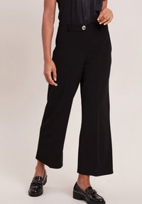 Zwarte wijde broek met een rechte taille, glanzende hardware in de taille en een gladde stof. Gecombineerd met zwarte loafers.