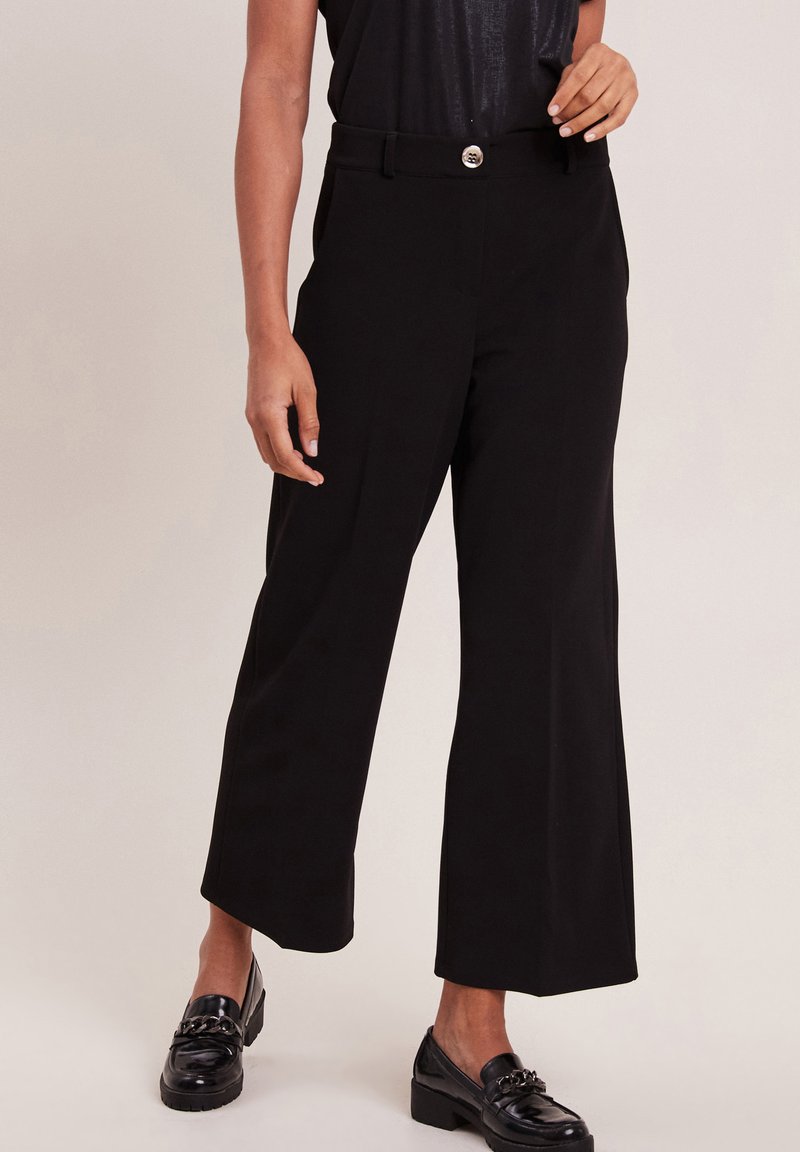 Zwarte wijde broek met een rechte taille, glanzende hardware in de taille en een gladde stof. Gecombineerd met zwarte loafers.