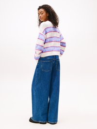 Fehér kötött pulóver geometrikus mintákkal és "tommy jeans" márkajellel, melyet bő szabású kék farmernadrággal párosítottak. Simább textúra, laza viselet.