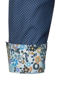 Pantaloni blu navy con piccoli pois bianchi e una riga a fantasia floreale nei colori blu, arancione e verde. Tessuto leggero con una consistenza liscia.