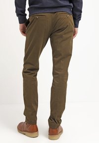 Hnědé chinos kalhoty s úzkým střihem, mají zadní kapsy a hladkou texturu. V kombinaci s hnědými botami má tento outfit neutrální barevnou paletu.