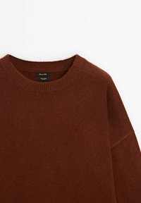 Pull en tricot marron avec un col rond, des bords côtelés et une coupe décontractée. Présente une texture subtile. Étiquette visible à l'intérieur.