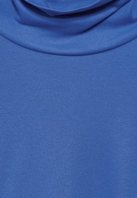 Blått tyg med en mjuk textur och design med draperad krage. Materialet verkar lätt och flexibelt, vilket gör det lämpligt för avslappnad användning.