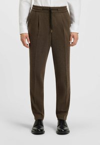 Bruine, op maat gemaakte broeken met een gestructureerd, hennepdesign. Voorzien van een elastische tailleband met een trekkoord en gestyled met zwarte schoenen.