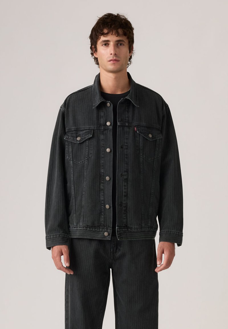 Μαύρο τζιν μπουφάν με κουμπιά μπροστά, δύο τσέπες στο στήθος και κάθετη ραβδωτή υφή. Μακριά μανίκια, άνετη εφαρμογή και ασημένια κουμπιά.