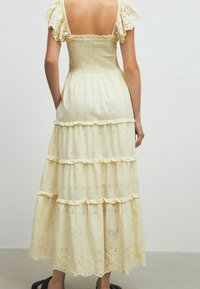 Robe maxi crème avec un corsage smocké, des manches courtes à volants, une jupe à étages et des détails en broderie anglaise sur l'ensemble du tissu.