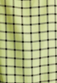 Grüner Stoff mit einem karierten Muster, in dem schwarze Linien Quadrate bilden. Die Textur wirkt glatt und gleichmäßig.
