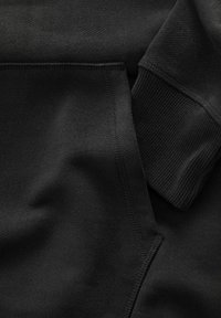 Gros plan sur la poche d'un sweat à capuche noir et le détail de la manche côtelée en tissu doux, mettant en valeur les coutures et la texture.