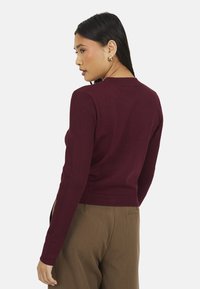 Pull rouge à côtes, �à manches longues, au design ajusté et au col rond, assorti à un pantalon taillé marron.