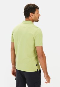 Poloshirt met korte mouwen in lichtgroen, met een kraag, zijsplitten en een gestructureerde stof. De achterkant toont een relaxte pasvorm.
