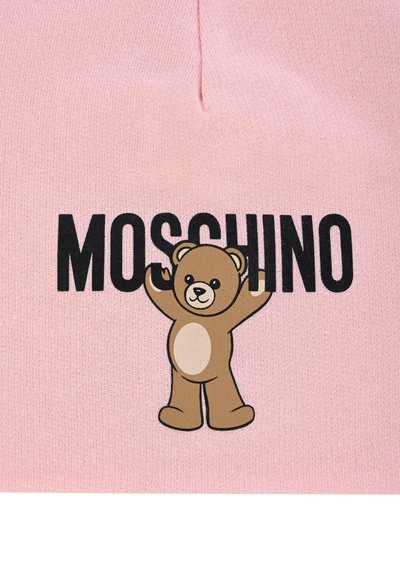 Vaaleanpunainen tekstiili, jossa on sarjakuvamainen karhukuva ja "MOSCHINO" paksuilla mustilla kirjaimilla karhun yläpuolella. Karhulla on vaaleanruskea turkki ja valkoinen vatsa.