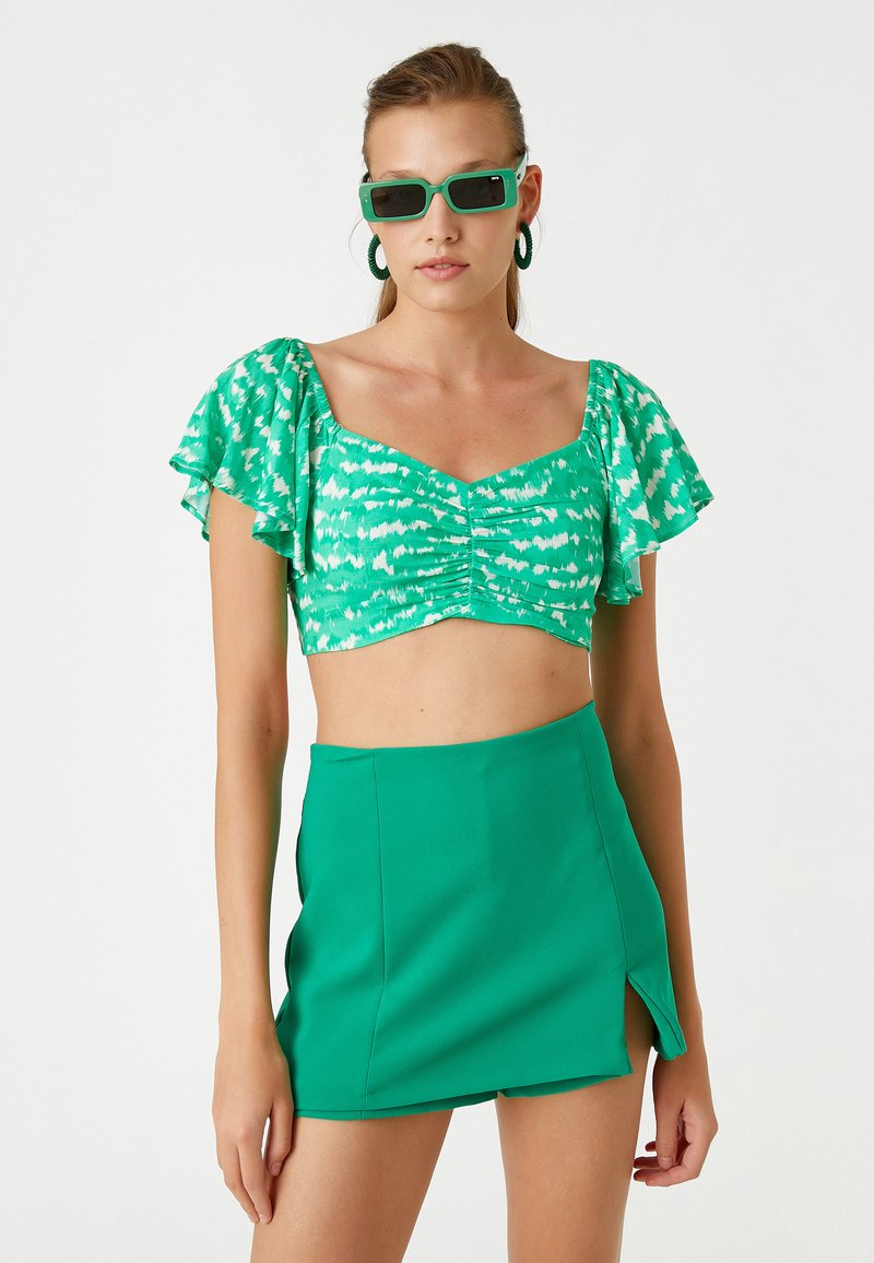 Zielony, wzorzysty crop top z krótkimi falbanurowymi rękawami i marszczonym przodem, w połączeniu z jednolitym zielonym mini spódnicą z bocznym rozcięciem.