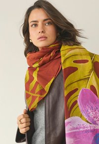 Kwadratowa apaszka w kolorach brązowym, żółtym i różowym. Z dużymi wzorami tropikalnych liści i motywami kwiatowymi. Wykonana z lekkiego materiału.