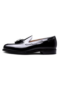 Black leather loafer with a smooth finish, featuring decorative stitching and a metal buckle accent. Rounded toe and low stacked heel.