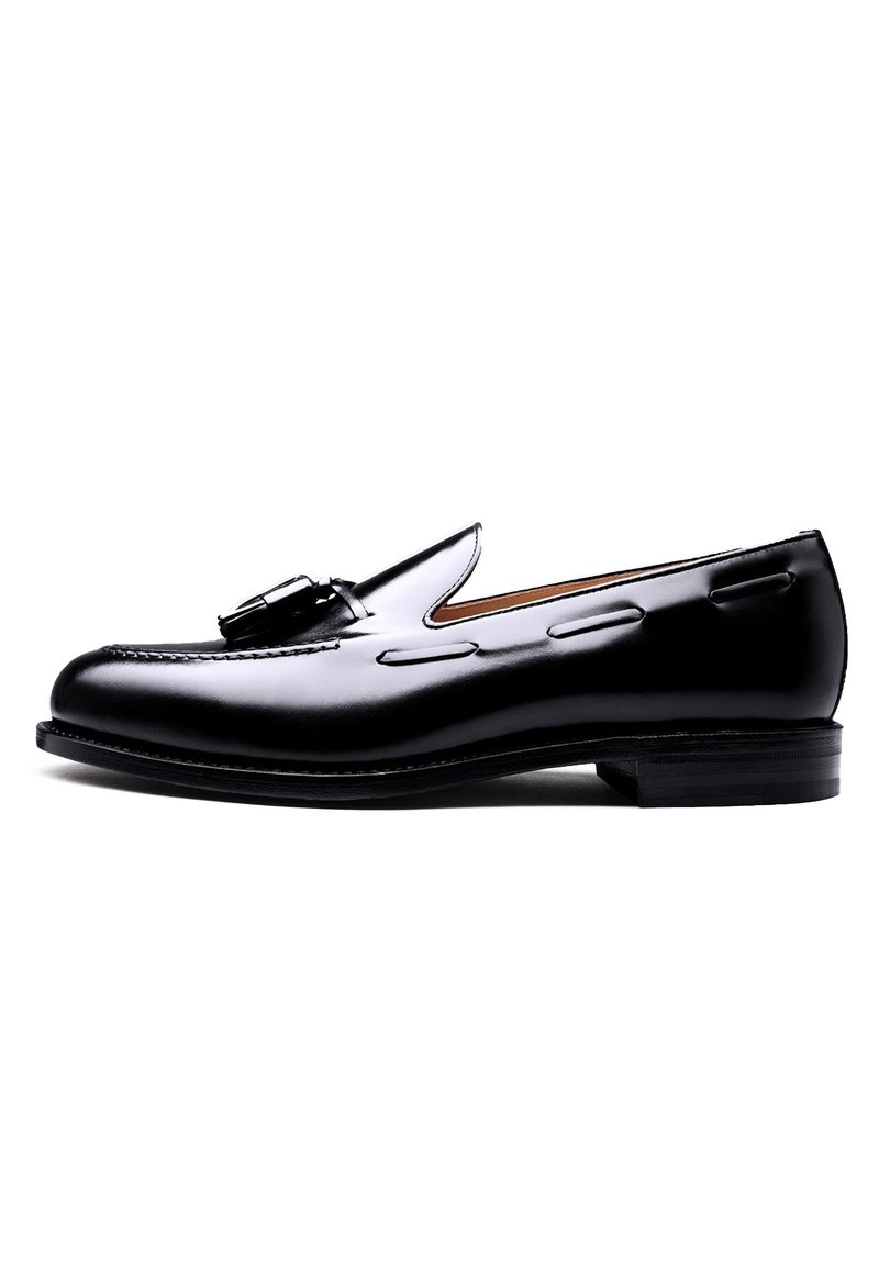 Black leather loafer with a smooth finish, featuring decorative stitching and a metal buckle accent. Rounded toe and low stacked heel.