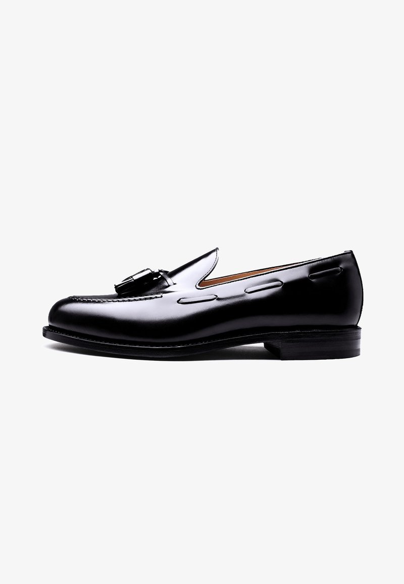 Black leather loafer with a smooth finish, featuring decorative stitching and a metal buckle accent. Rounded toe and low stacked heel.