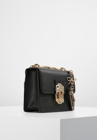 Czarna syntetyczna torebka o strukturalnym designie, ze złotymi elementami, kwiatowymi zdobieniami oraz łańcuszkowym paskiem, z klapą i zapięciem na zamek z przodu.