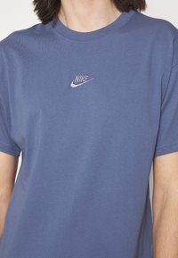 Camiseta de algodón azul con cuello redondo y mangas cortas, que presenta un pequeño logo de Nike bordado en blanco en el pecho. Textura suave.